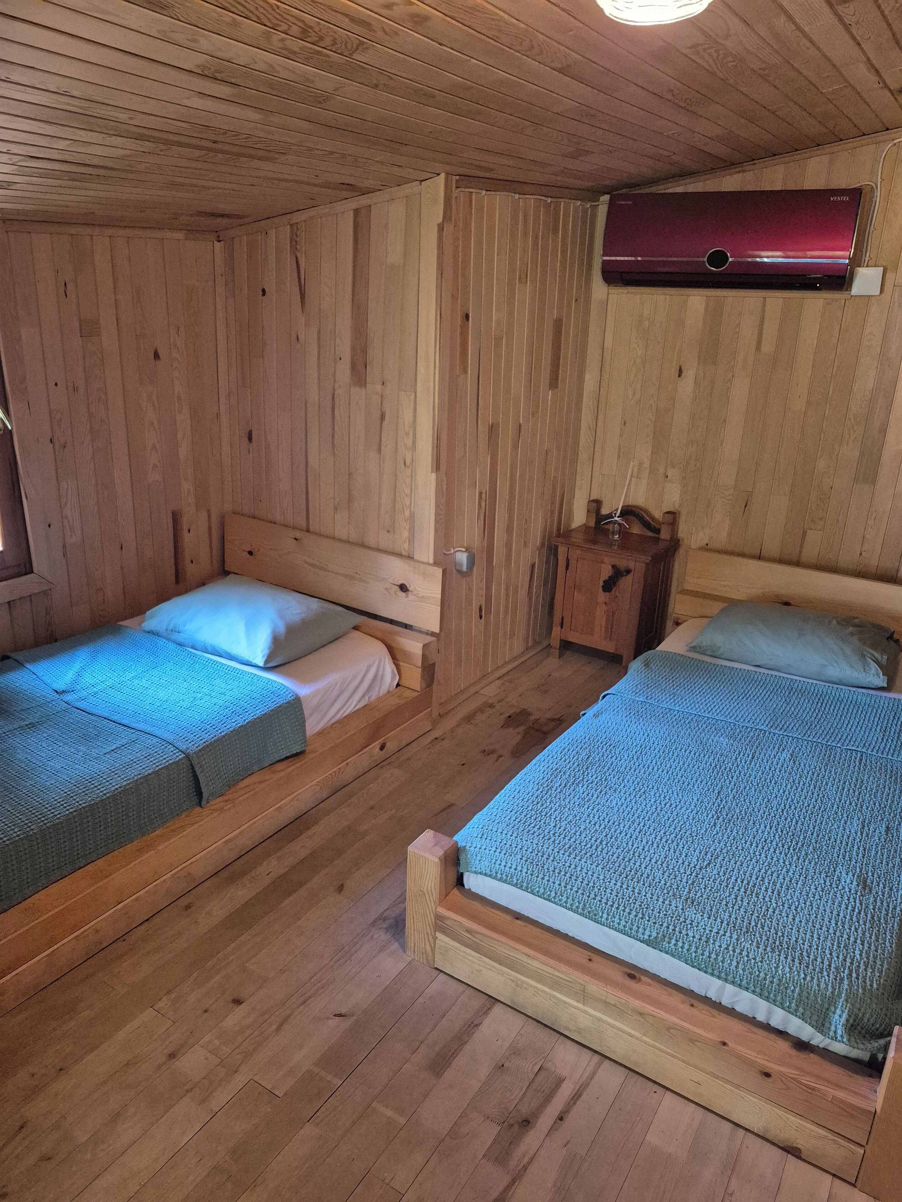 Ein Zimmer aus Holz mit zwei Betten, einem Heizgerät und einem kleinen Holzschrank.