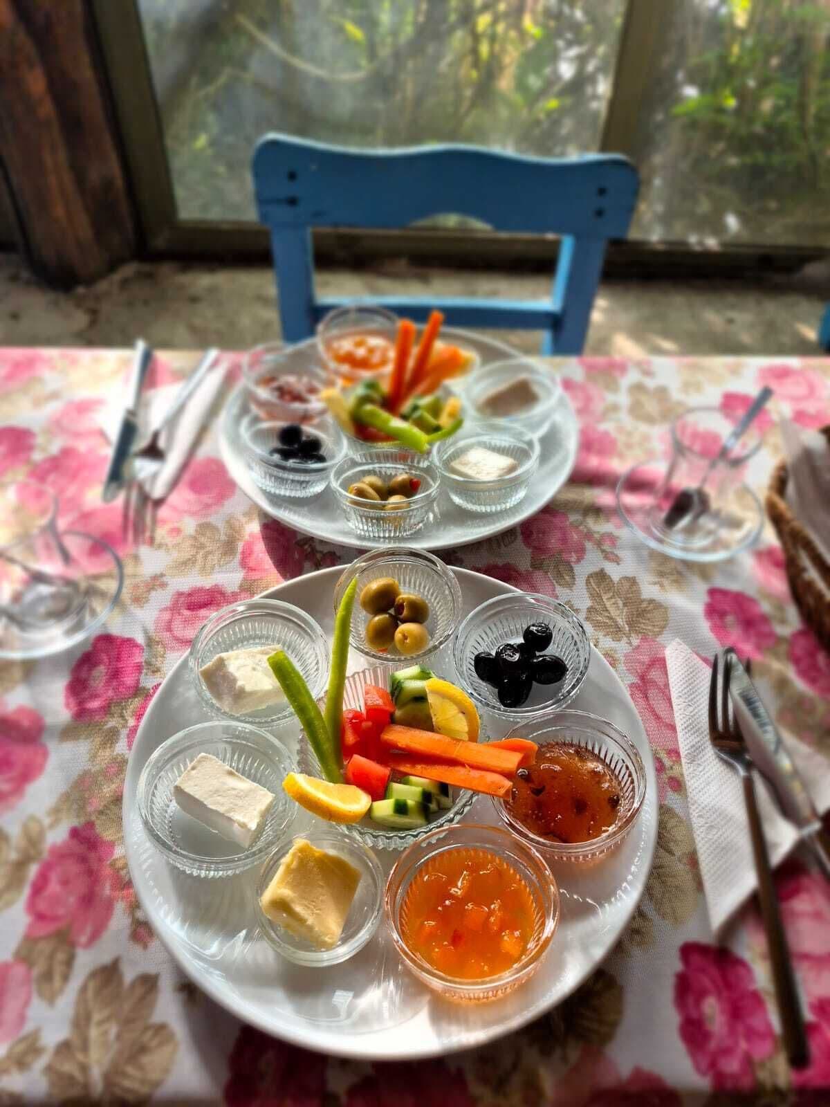Une table recouverte d’une nappe à motifs floraux, deux assiettes remplies de nourriture et une chaise bleue.