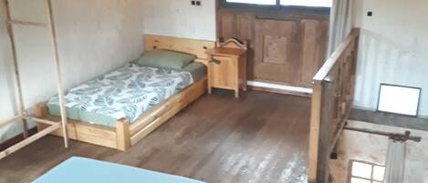 A rustic wooden room with a loft bed, a small wooden table, and a window with curtains.
