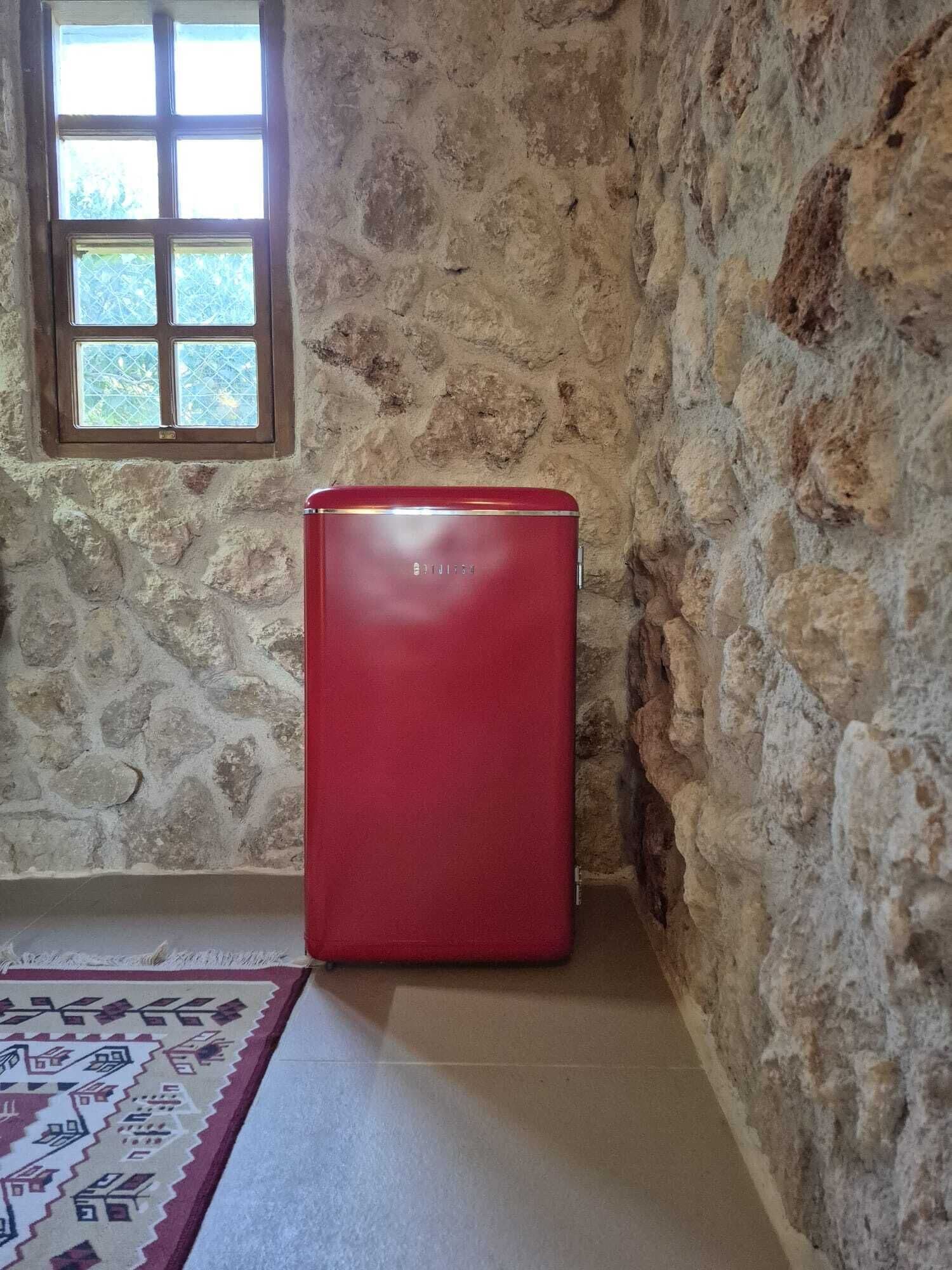 Una maleta roja en un rincón de una habitación con paredes de piedra y una ventana.