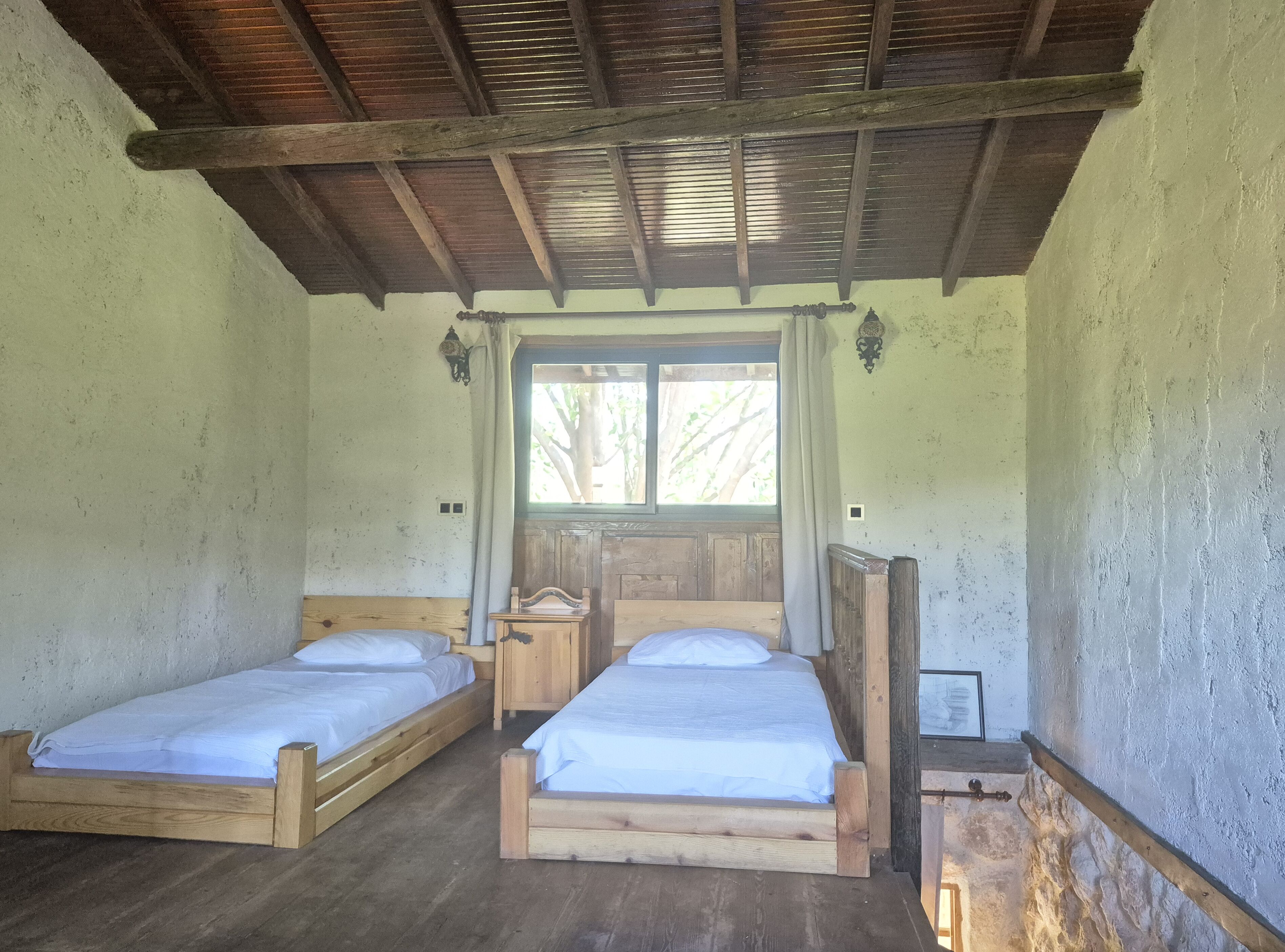 Een rustieke kamer met twee houten bedden, een raam met gordijnen en een houten plafond.