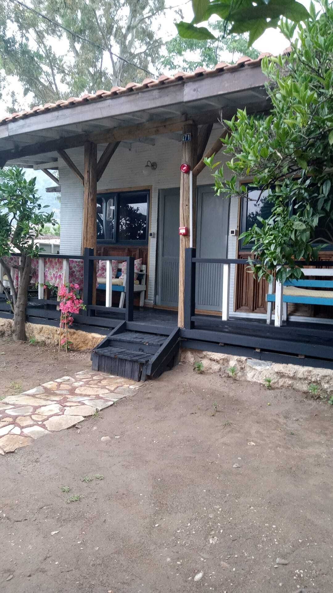 Un porche cubierto con un sendero de piedra que lleva a un banco de madera, un árbol pequeño con flores rosadas y una cerca de madera.
