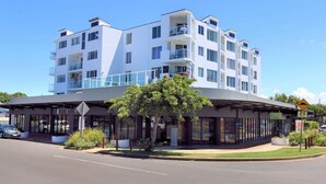 Um hotel moderno de vários andares com área externa coberta, placa de limite de velocidade e uma árvore na frente.