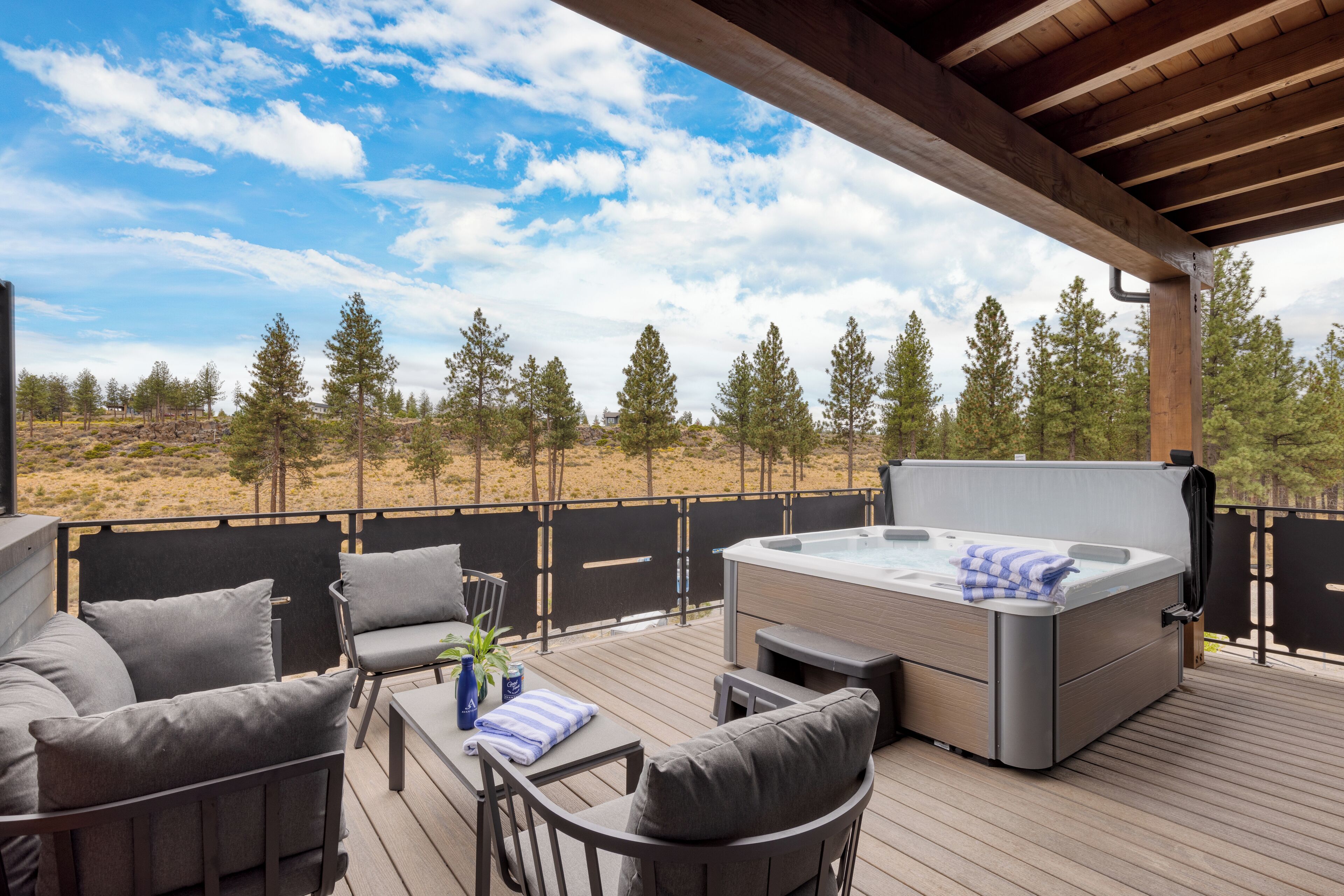 An outdoor deck with a hot tub, seating area, and a view of a forested landscape.