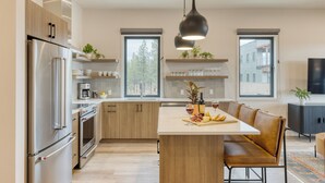 Una cocina moderna con una isla central, electrodomésticos de acero inoxidable, armarios de madera y ventanas amplias.