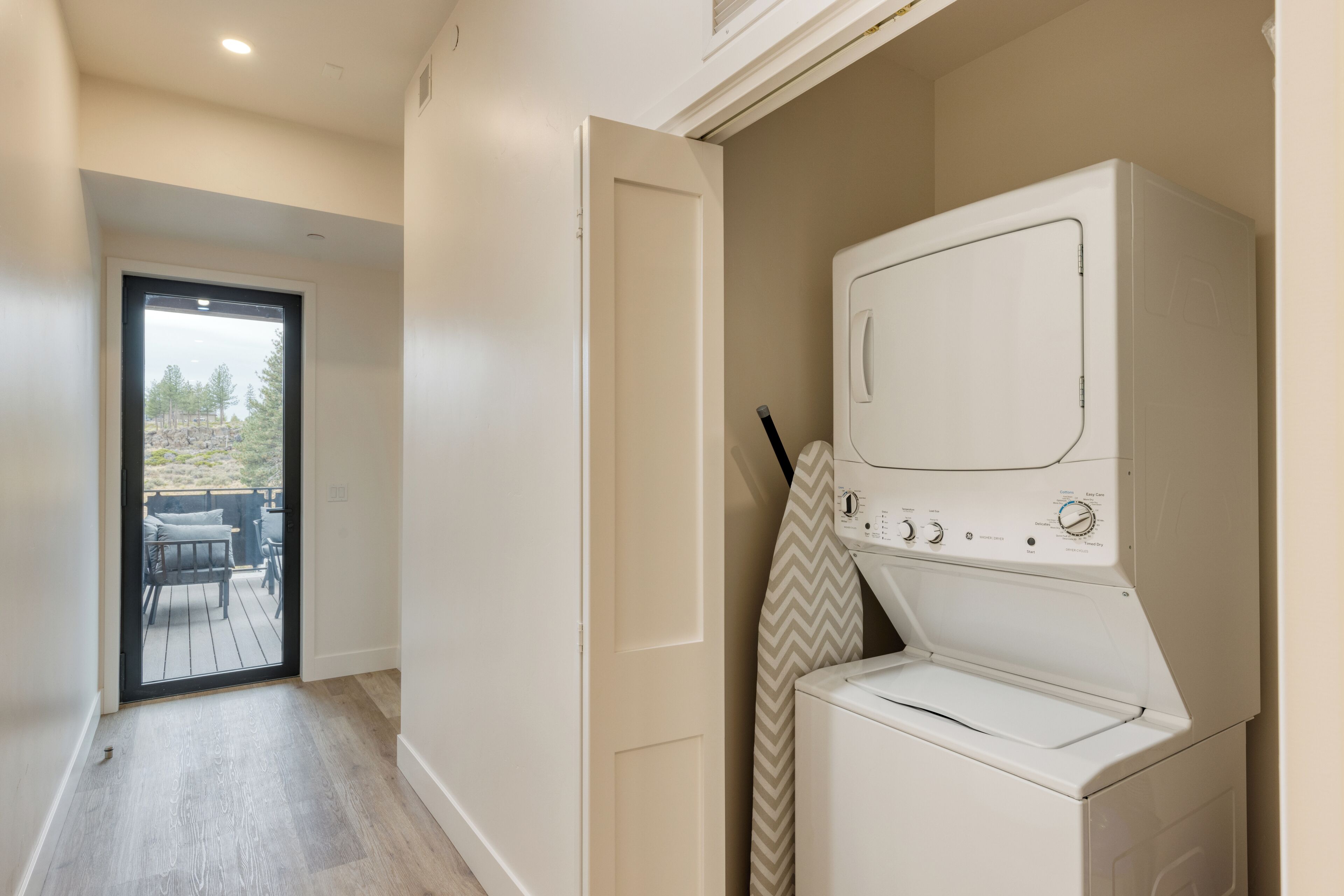 A laundry room with a washer and dryer, a door leading to a balcony, and a view of the outdoors.