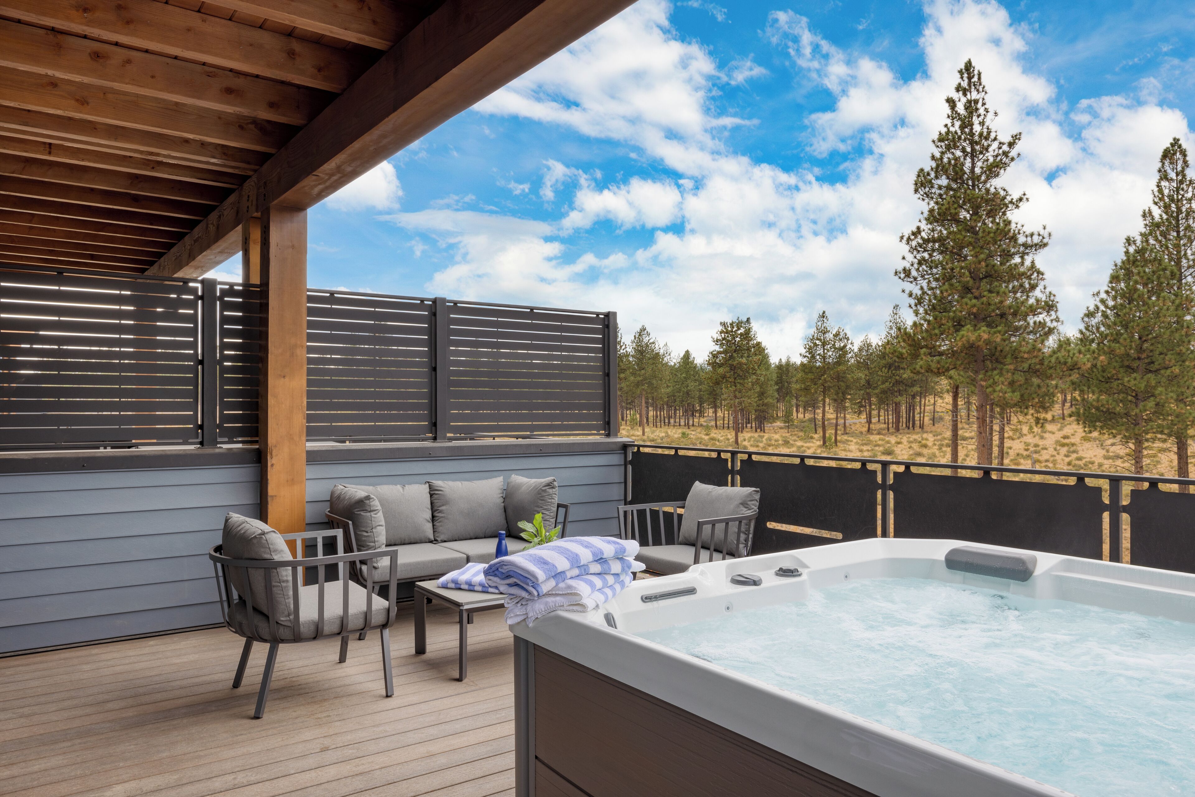 A wooden deck with a hot tub, seating area, and a view of trees and sky.