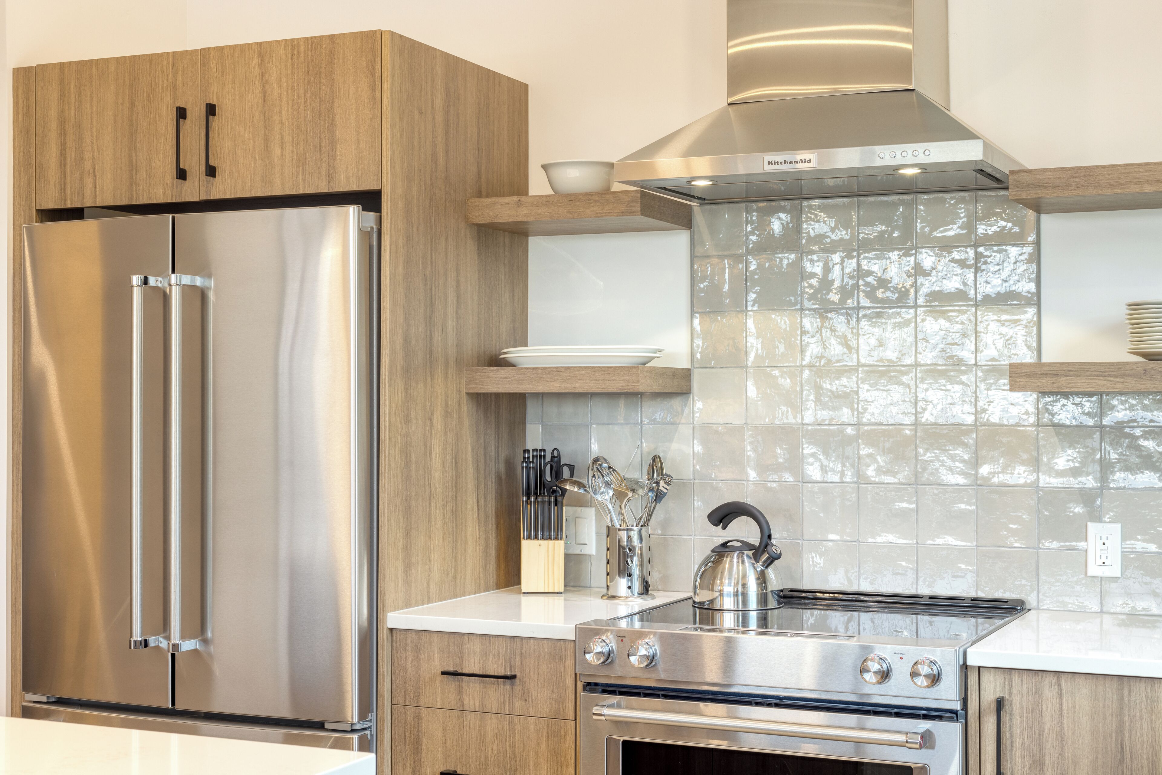 A modern kitchen with stainless steel appliances, wooden cabinets, and a tiled backsplash.