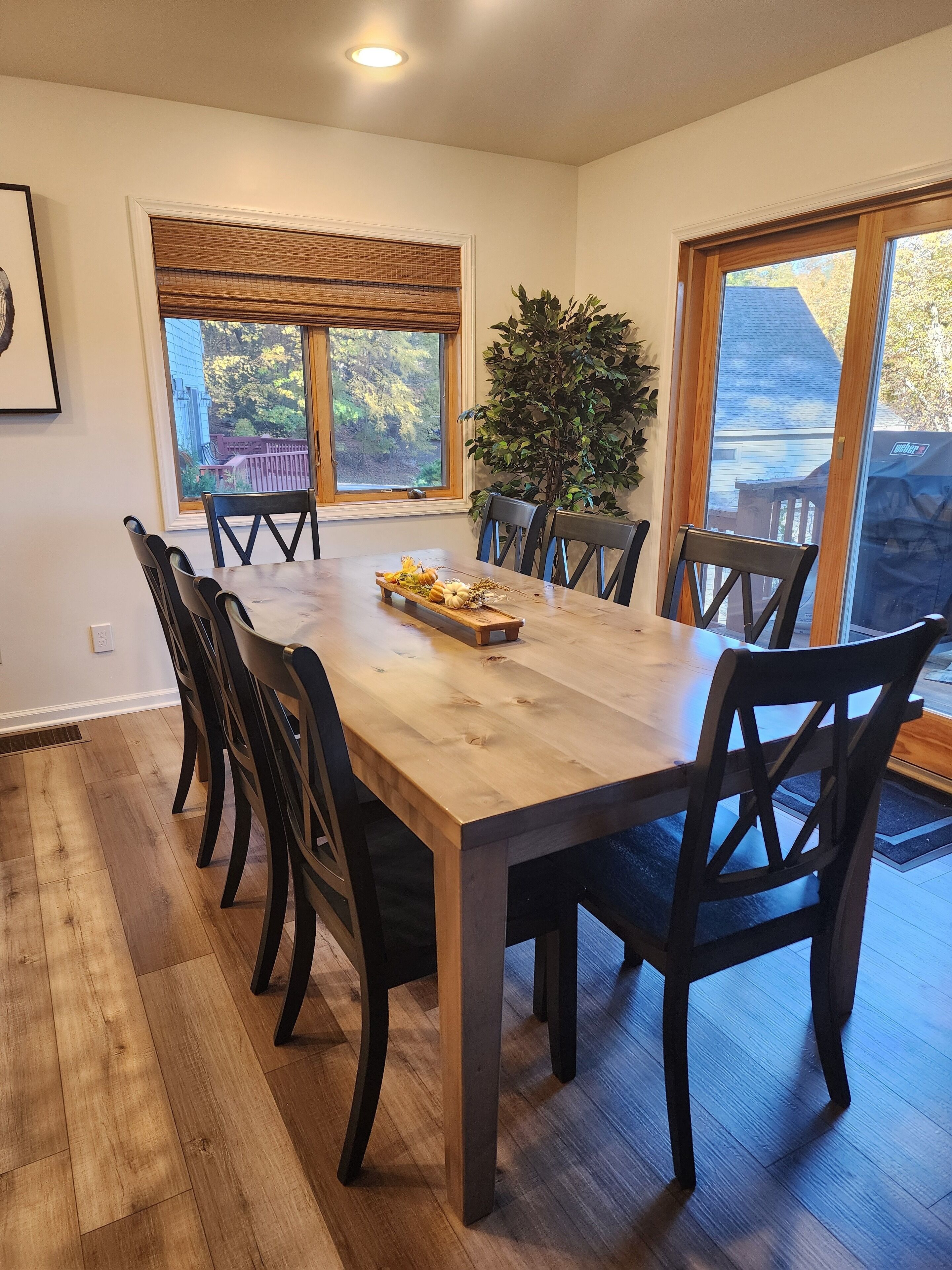 A dining room with a large wooden table, black chairs, and a potted plant.