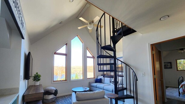 Un amplio salón con una escalera moderna, ventanas grandes y una acogedora disposición de asientos.