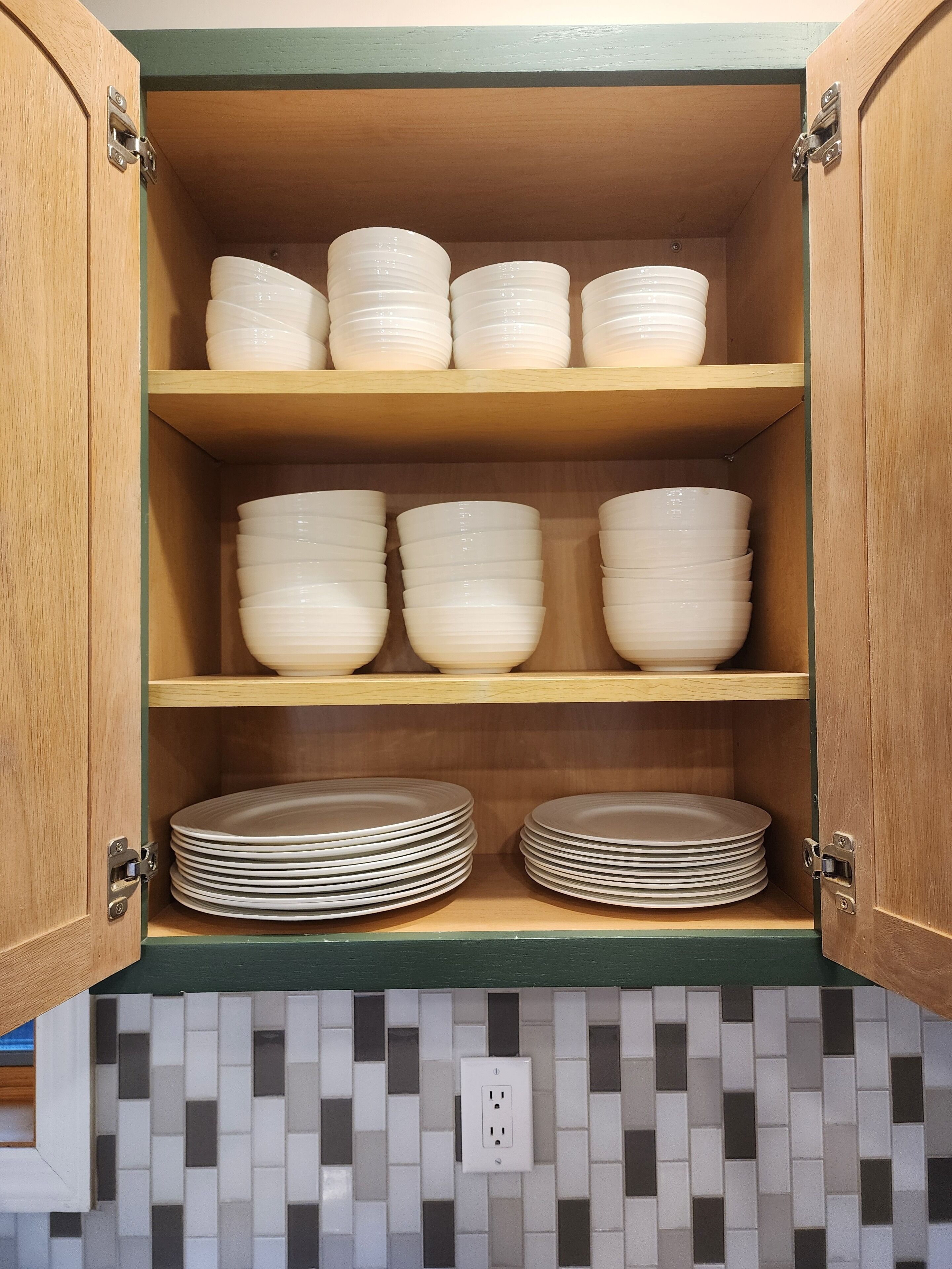 Un meuble de cuisine doté de trois étagères, chacune contenant des piles de bols et d’assiettes blancs.