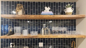 Una cocina con dos estantes de madera, salpicadero de baldosas negras, un lavamanos y una encimera.