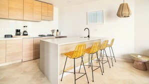 Una cocina moderna con armarios de madera, una isla central con taburetes de bar, una lámpara colgante y una pequeña mesa redonda con una vela.