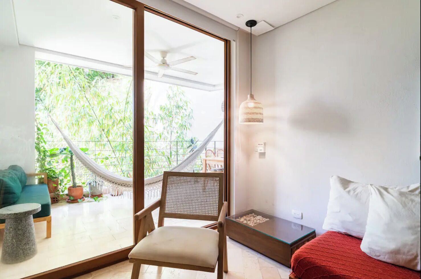 A modern living room with a hammock, a wooden chair, a red sofa, and a glass coffee table.