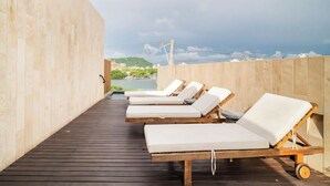 Terraza de madera con cuatro tumbonas mirando un cuerpo de agua y un paisaje montañoso.