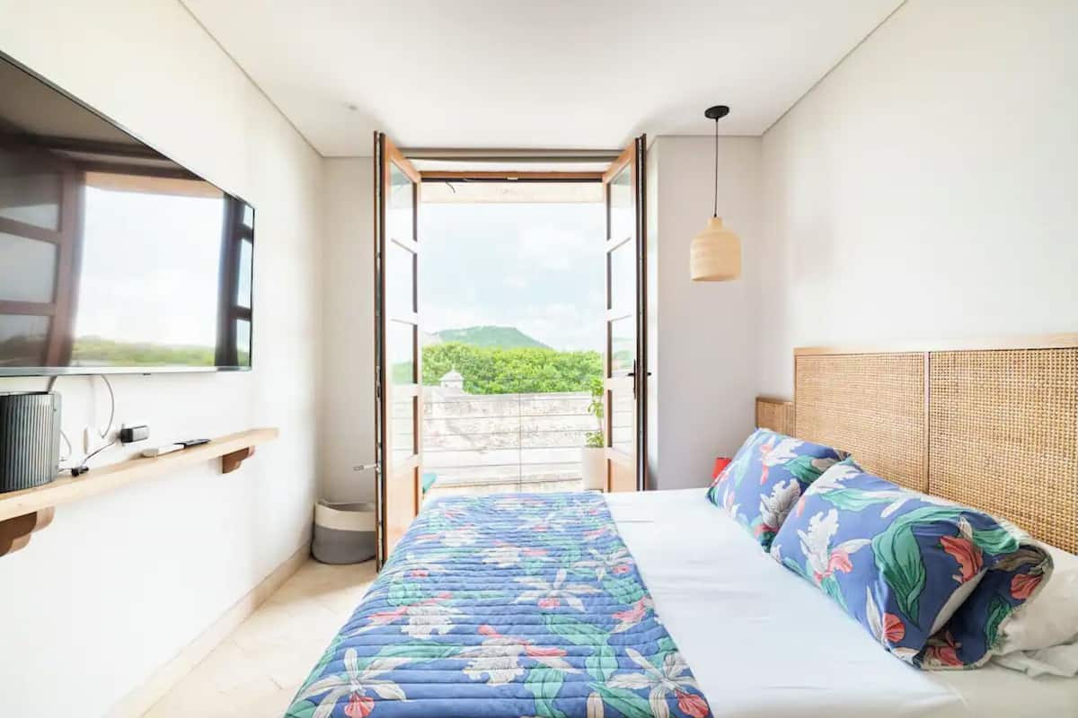 Un dormitorio con cama, televisor, ventana y balcón con vista a follaje.