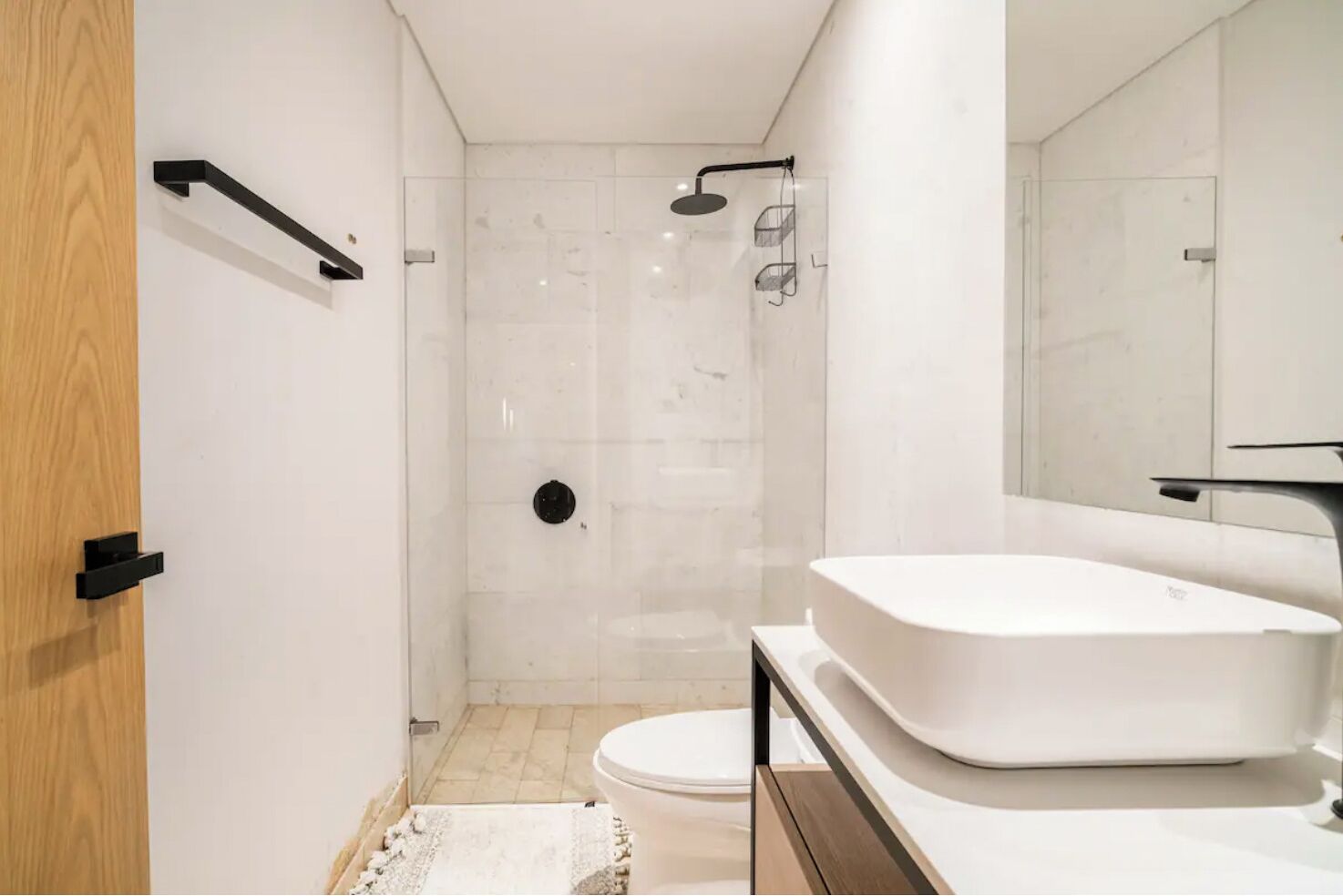 A modern bathroom with a white sink, a shower, and a wooden door.