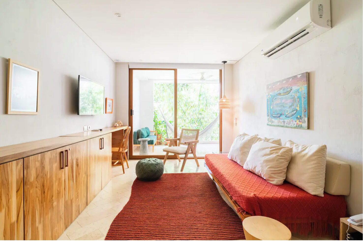 A modern living room with a sofa, a dining area, and a view of greenery through the glass door.