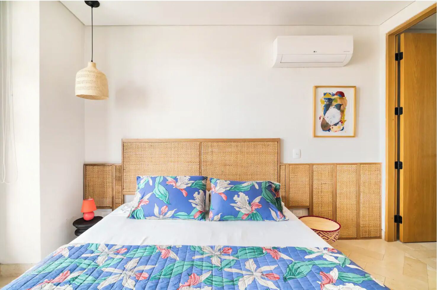 A bedroom with a bed, a hanging light, a wall-mounted air conditioner, and a door.