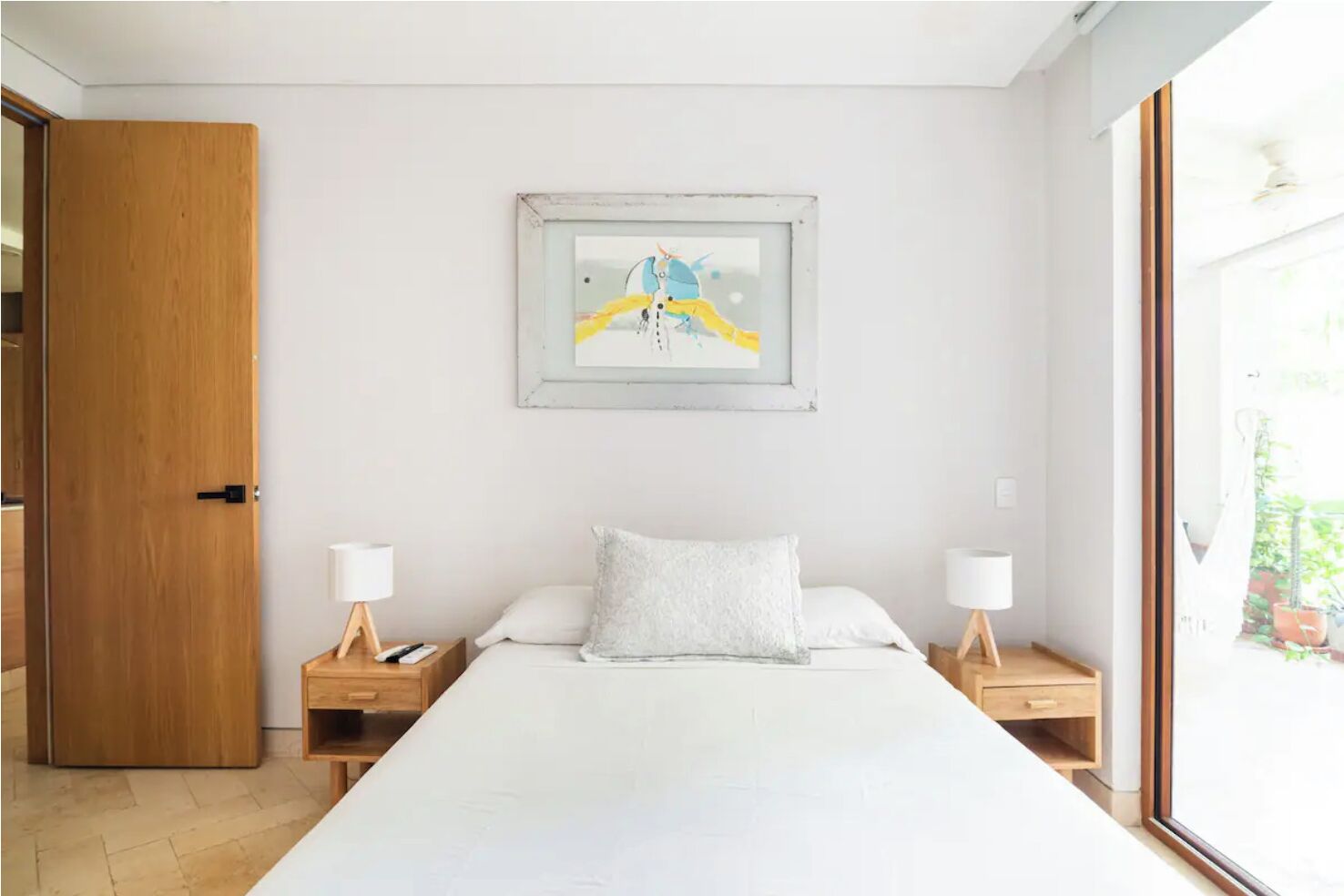 A bedroom with a large bed, two bedside tables, a nightstand, a wooden door, and a framed picture on the wall.