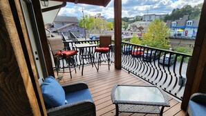 A wooden deck with wicker furniture, a glass table, and a view of the town. - The Loft at the Old Mill-Cozy 2-bedroom Loft in charming Pigeon Forge! (Pigeon Forge)