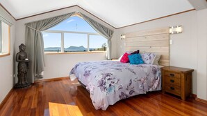 Une chambre avec un grand lit, une tête de lit en bois, une statue et une vue sur l’extérieur.