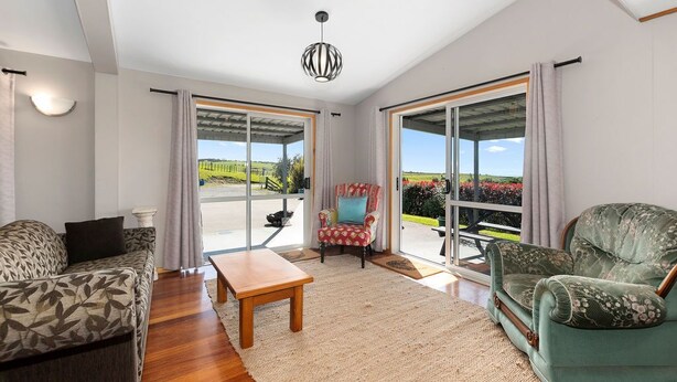 Un salon spacieux comprenant un canapé, un fauteuil et une table. De grandes portes-fenêtres coulissantes donnent accès à un balcon offrant une vue sur la verdure.