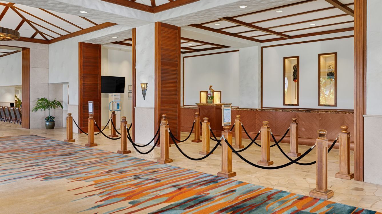 A hotel lobby with a patterned carpet, wooden columns, and a reception desk.