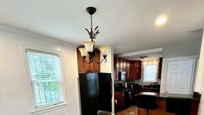 A modern kitchen with a black refrigerator, wooden cabinets, and a glass dining table with metal chairs. - Charming 3-bedroom house by Capitol Hill DC (Washington)