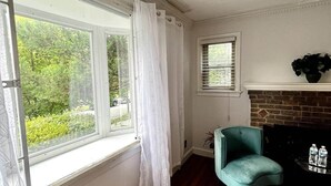 A room with a fireplace, a teal armchair, and a window with white curtains. - Charming 3-bedroom house by Capitol Hill DC (Washington)