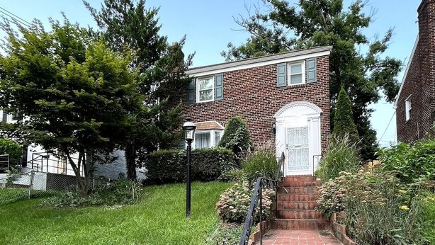 A brick staircase leading to a white door with a decorative design, surrounded by a well-maintained garden and a clear blue sky. - Charming 3-bedroom house by Capitol Hill DC (Washington)