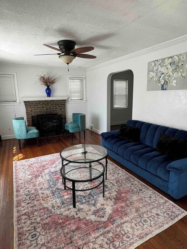 A living room with a blue sofa, two armchairs, a fireplace, a ceiling fan, and a patterned rug. - Charming 3-bedroom house by Capitol Hill DC (Washington)