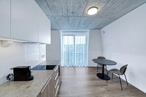 A modern kitchen with a built-in stove, a dining area with a round table and two chairs, and a large window with sheer curtains. - Mooi Apartments Biel (Biel)