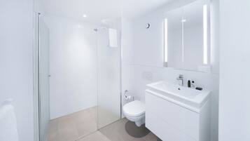 Ein modernes Badezimmer mit Duschabtrennung aus Glas, einer weißen Toilette und einem Waschtisch mit Spiegel und Waschbecken.