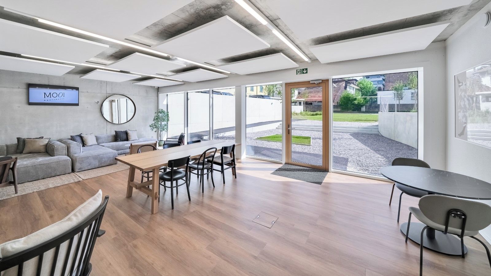 Un espace de bureau moderne avec une grande table en bois, plusieurs chaises, un canapé et un écran de télévision affichant le mot « MOOI ».