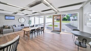 Un espace de bureau moderne avec une grande table en bois, plusieurs chaises, un canapé et un écran de télévision affichant le mot « MOOI ».