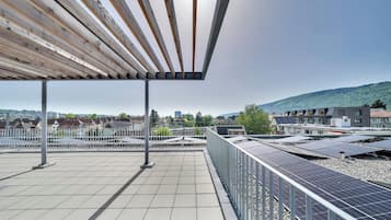 A rooftop terrace with solar panels, a pergola, and a view of a cityscape and hills.