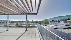 A rooftop terrace with solar panels, a pergola, and a view of a cityscape and hills. - Mooi Apartments Biel (Biel)