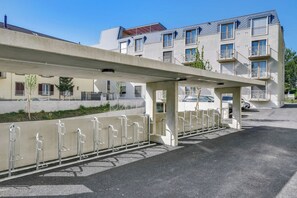 A parking area with a covered walkway, metal railings, and a row of parked cars. - Mooi Apartments Biel (Biel)