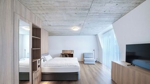 A modern bedroom with a bed, built-in wardrobe, bedside table, lamp, and a TV. - Mooi Apartments Biel (Biel)
