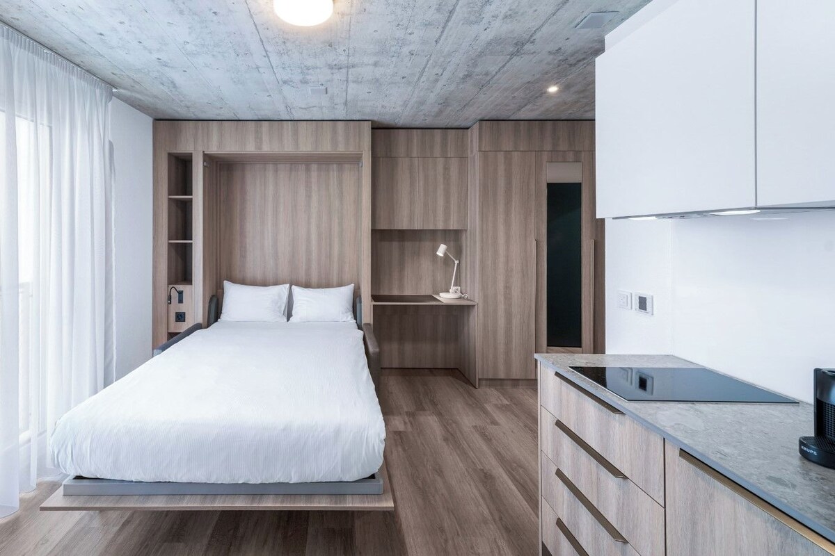 A modern bedroom with a bed, bedside table, and a built-in desk with a lamp.