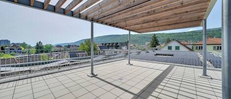 Eine Dachterrasse mit einer Holzpergola, Fliesenboden und Blick auf Gleise und umliegende Gebäude.