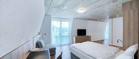 A modern bedroom with a bed, a desk, a chair, a TV, and a large window.