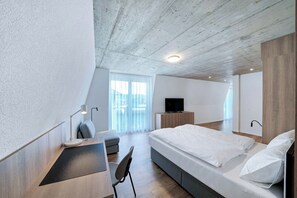 A modern bedroom with a bed, a desk, a chair, a TV, and a large window. - Mooi Apartments Biel (Biel)