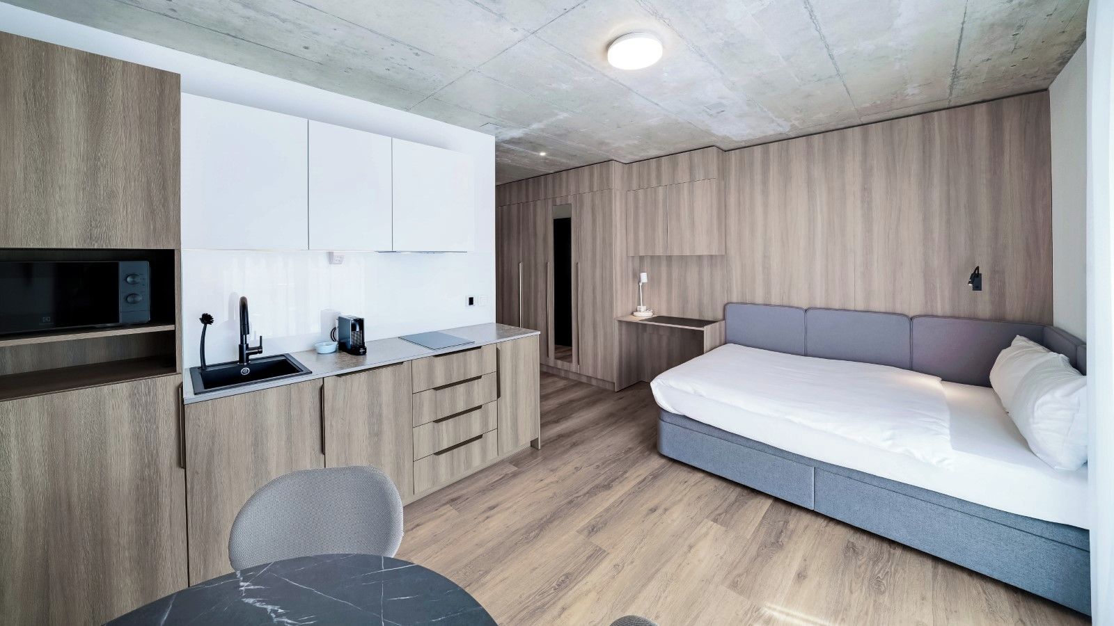 Ein kompaktes Hotelzimmer mit Küchenzeile, einem Bett und einer Sitzecke.