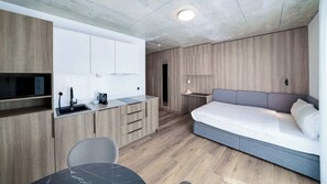 A compact hotel room with a kitchenette, a bed, and a seating area. - Mooi Apartments Biel (Biel)