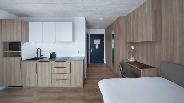Une chambre d’hôtel moderne équipée d’une kitchenette, d’un lit, d’un bureau et d’une chaise.