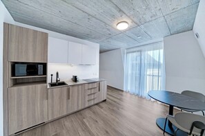 A modern kitchen with wooden cabinets, a built-in microwave, and a dining area with a table and chairs. - Mooi Apartments Biel (Biel)