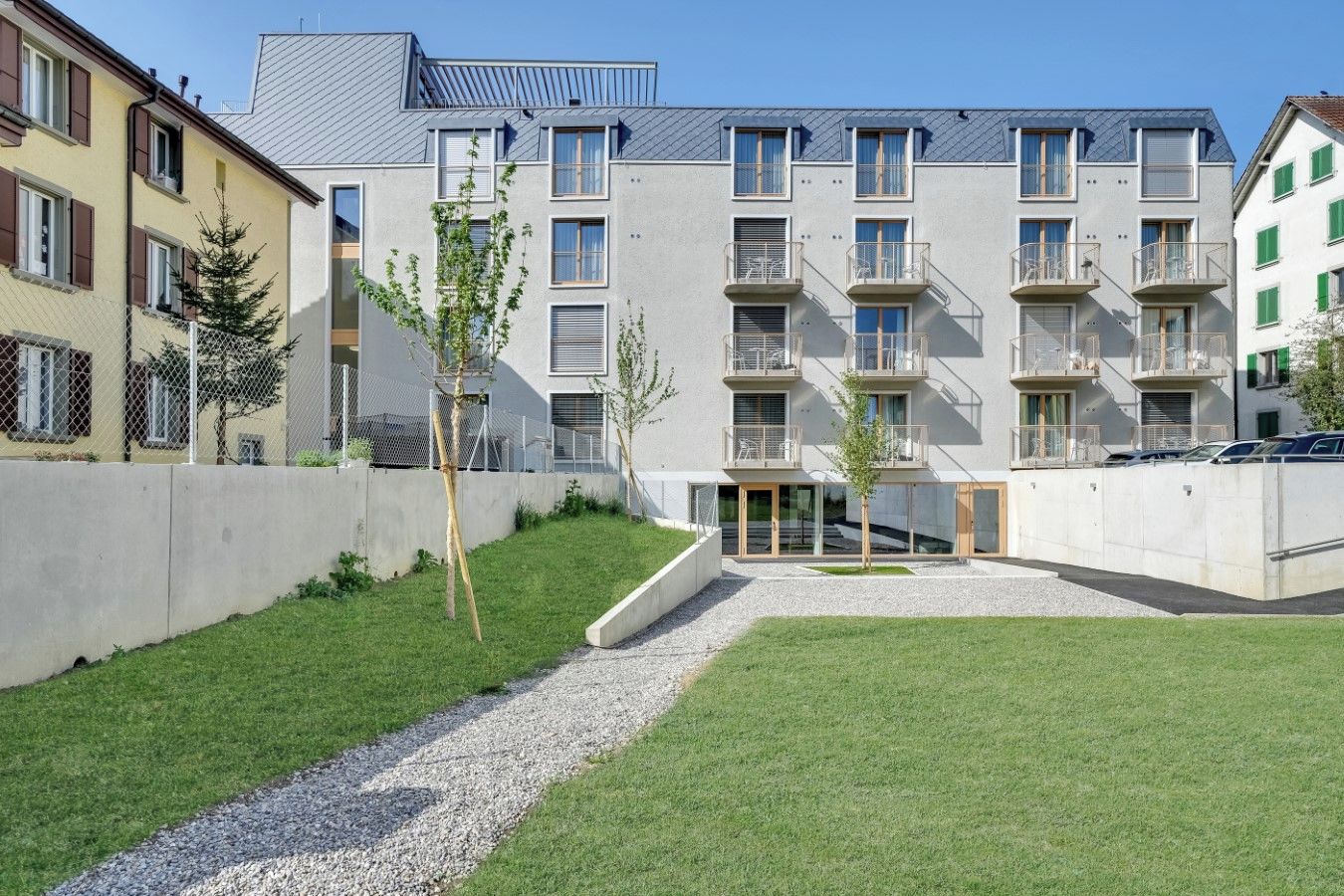 Un moderno edificio de apartamentos con varios balcones y un patio central con un camino de grava.