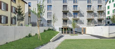 Un moderno edificio de apartamentos con varios balcones y un patio central con un camino de grava.
